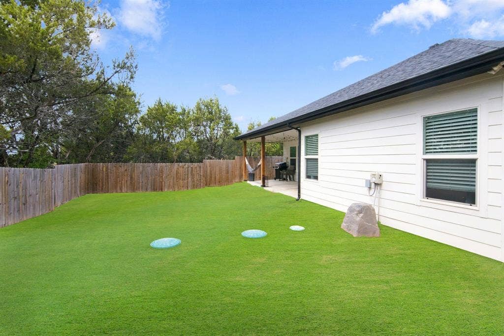 4822 Wichita Street, Granbury, TX 76048 Spacious fenced backyard featuring a covered patio, broad lawn, and mature perimeter trees