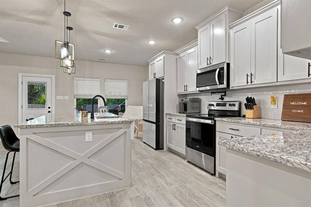 4822 Wichita Street, Granbury, TX 76048 Kitchen featuring white shaker cabinetry, stainless steel appliances, light-toned granite countertops, and wood-finish flooring