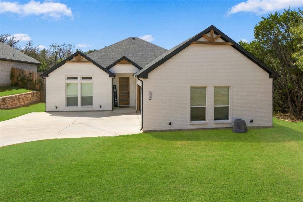 4822 Wichita Street, Granbury, TX 76048 White brick exterior with dark trim, featuring a dark shingle roof and a concrete driveway