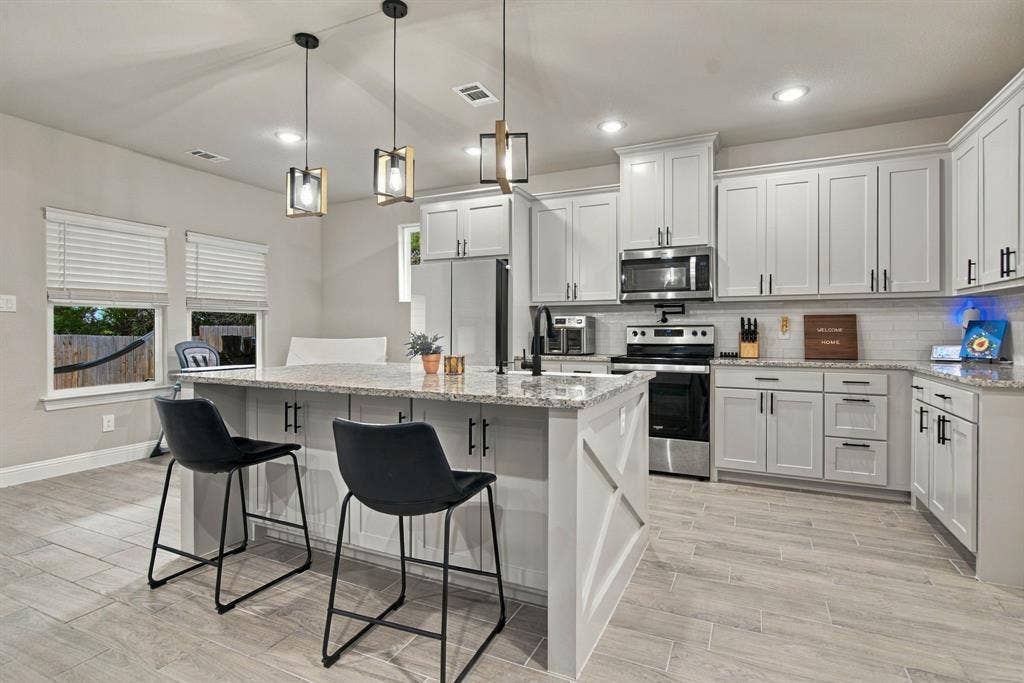 4822 Wichita Street, Granbury, TX 76048 Kitchen featuring stainless steel appliances, light gray cabinetry, a central island with a granite countertop, and wood-finish flooring