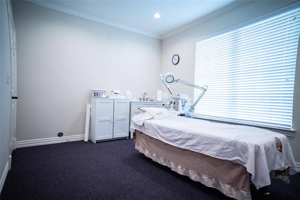 8668 John Hickman Parkway, #906, Frisco, TX 75034 Professional treatment room featuring recessed ceiling lighting, white cabinetry with ample storage, dark carpeted flooring, horizontal window treatments providing privacy control, and a treatment table with adjustable overhead lamp for task lighting