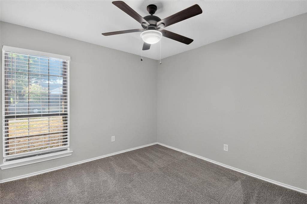 Neutral gray walls, dark gray carpet, white window trim, horizontal blinds, and a ceiling fan with integrated lighting