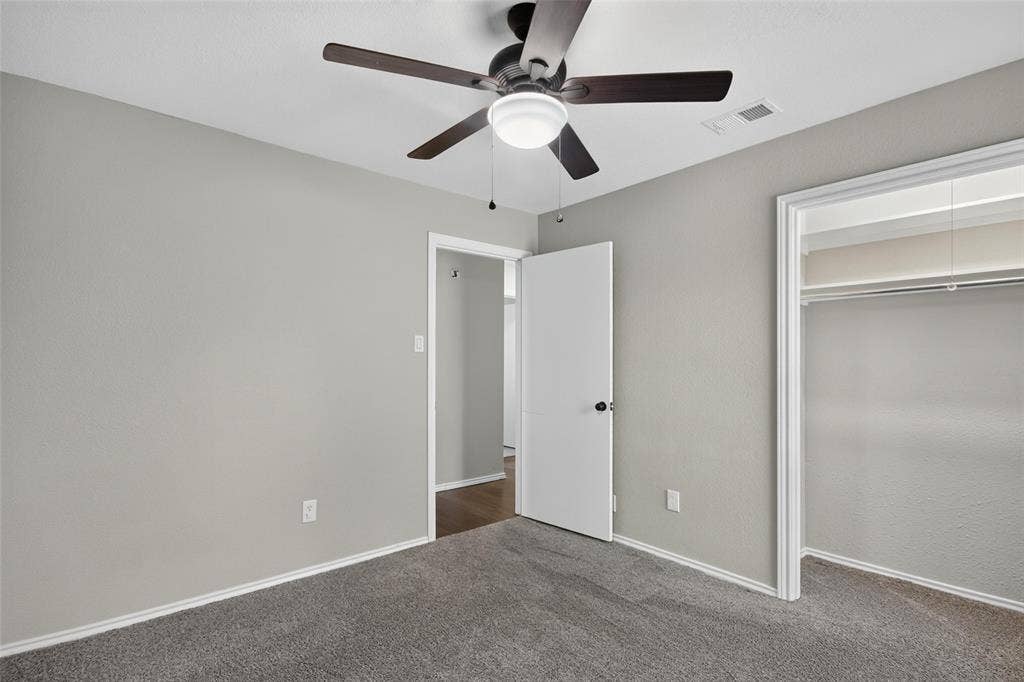 Plush grey carpet flooring, light grey painted walls, ceiling fan with integrated lighting, and a closet with a built-in hanging rod