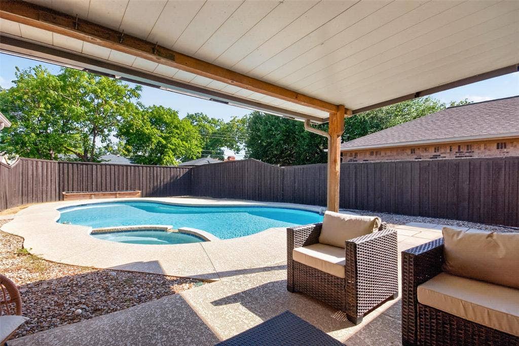 Covered patio with exposed wood beam supports, concrete decking, and a built-in swimming pool featuring an integrated spa