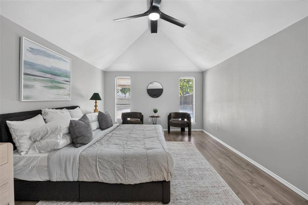 Vaulted ceiling, wood-finish flooring, two windows with blinds, and a ceiling fan with integrated lighting