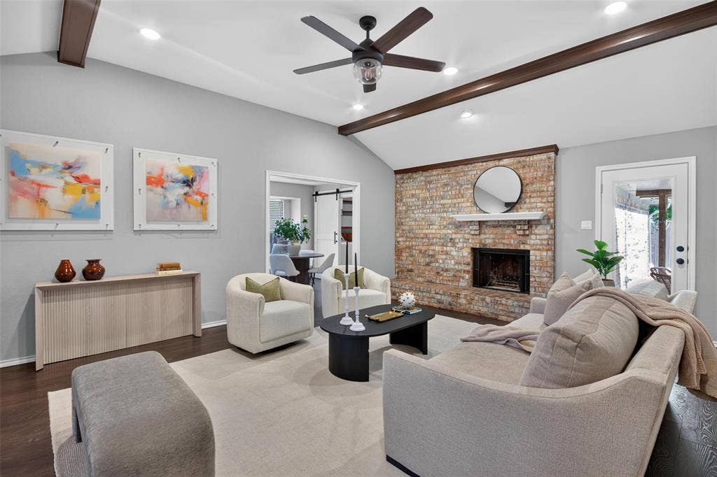 Vaulted ceiling with exposed wood beams, brick fireplace with mantel, dark wood-finish flooring, recessed lighting, and a ceiling fan