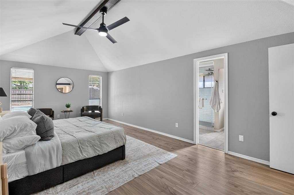Vaulted ceiling with exposed beam, ceiling fan, wood-finish flooring, and a bathroom entrance with tiled flooring