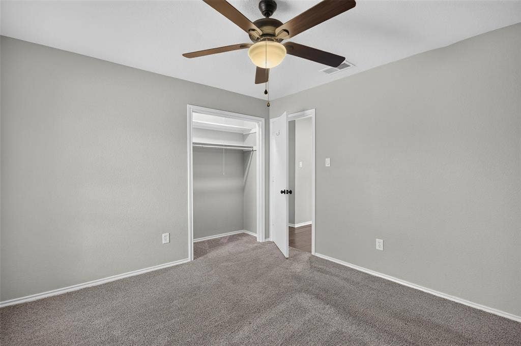 Neutral tone walls, ceiling fan with integrated lighting, gray carpeting, and a built-in closet with shelving