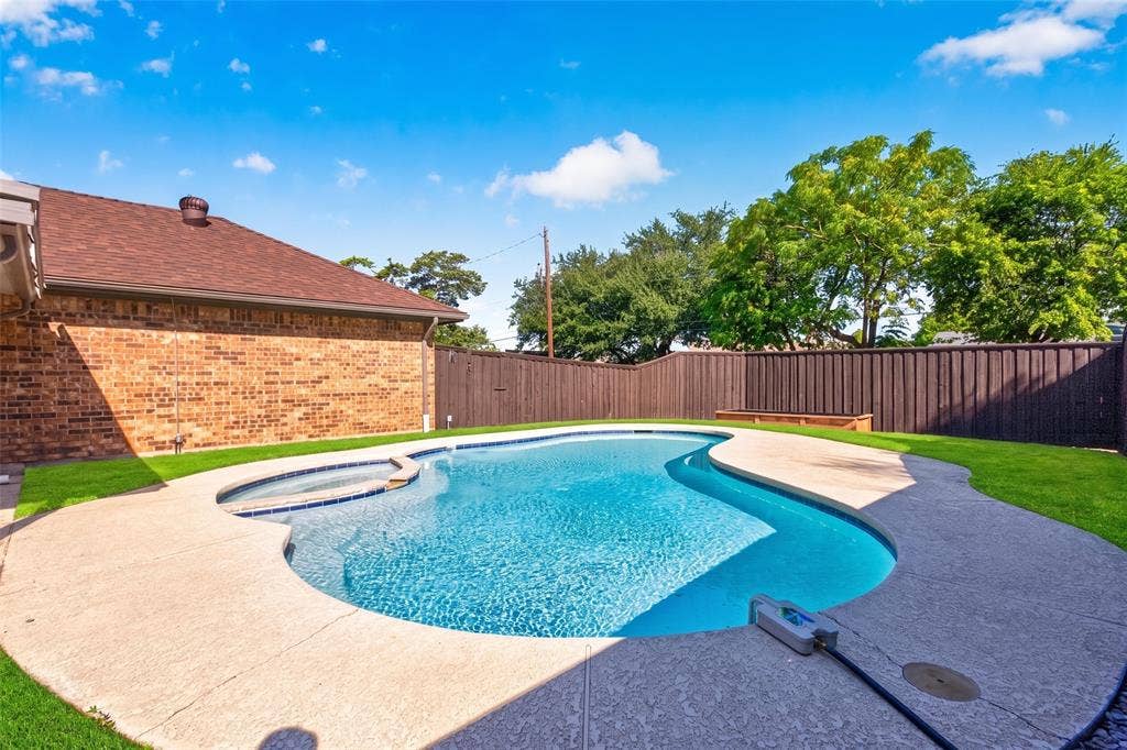 In-ground swimming pool with integrated spa, expansive concrete decking, and perimeter fencing