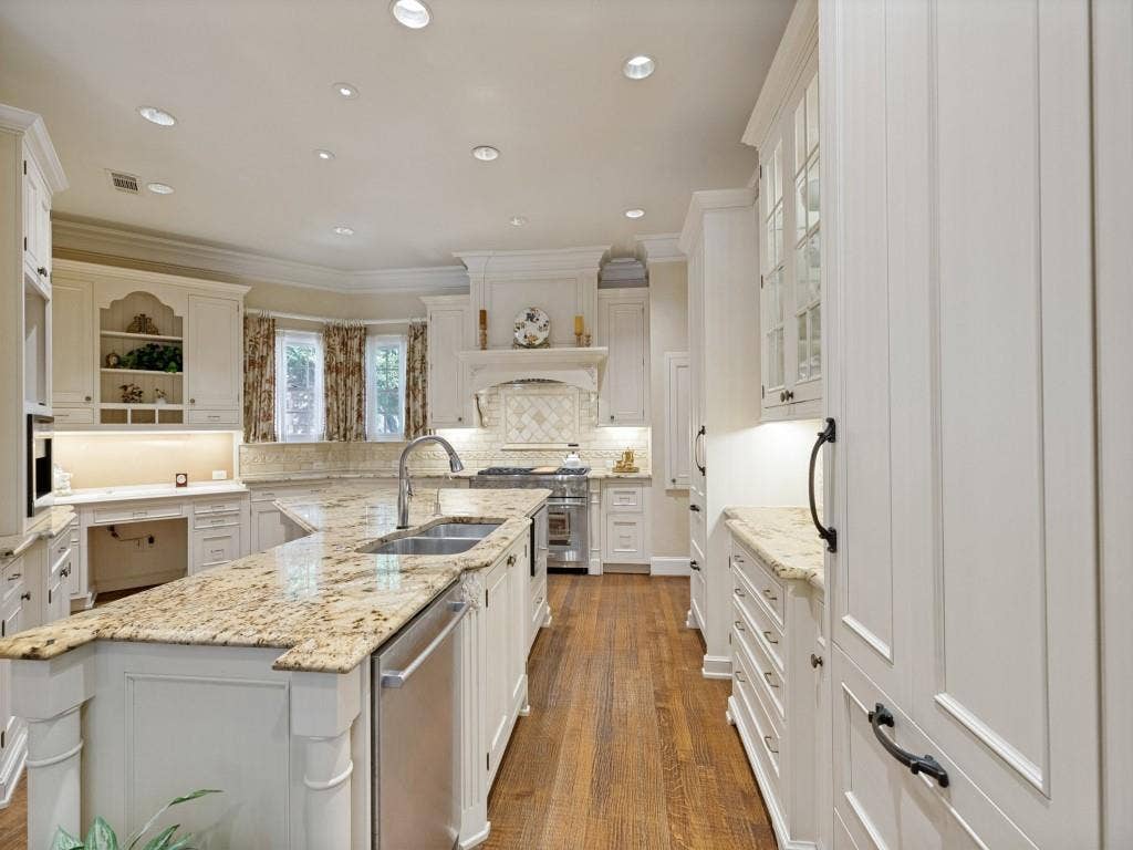 Kitchen featuring a large island with an undermount sink, light-toned countertops, white cabinetry with dark hardware, and wood-finish flooring