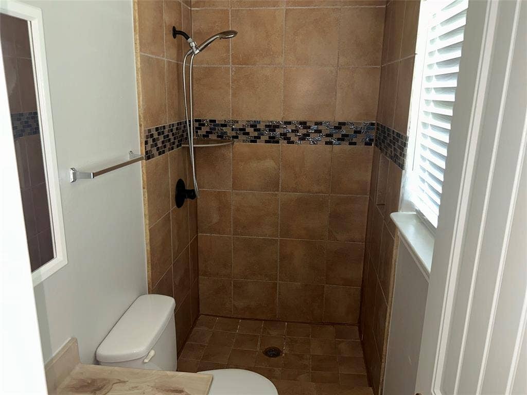 3602 Palm Drive, Mesquite, TX 75150 Tiled shower stall featuring a decorative mosaic accent band, built-in shelf, and handheld shower fixture