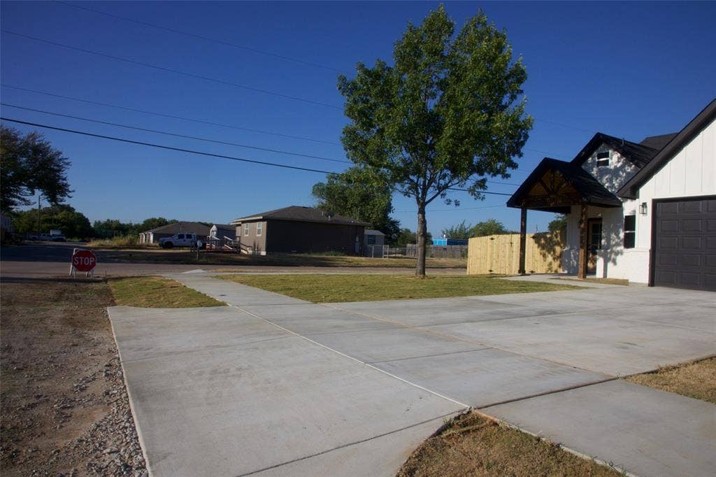 9432 PRAIRIEVIEW Drive, Crowley, TX 76134 Expansive concrete driveway, attached garage with a dark panel door, white exterior siding, covered entry porch with exposed wood beams, and a mature tree