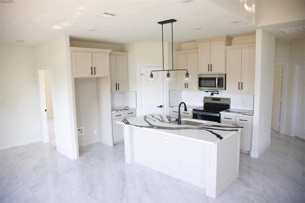 9432 PRAIRIEVIEW Drive, Crowley, TX 76134 Contemporary kitchen featuring a center island with a large sink and faucet, white cabinetry with dark hardware, stainless steel microwave, and integrated cooktop