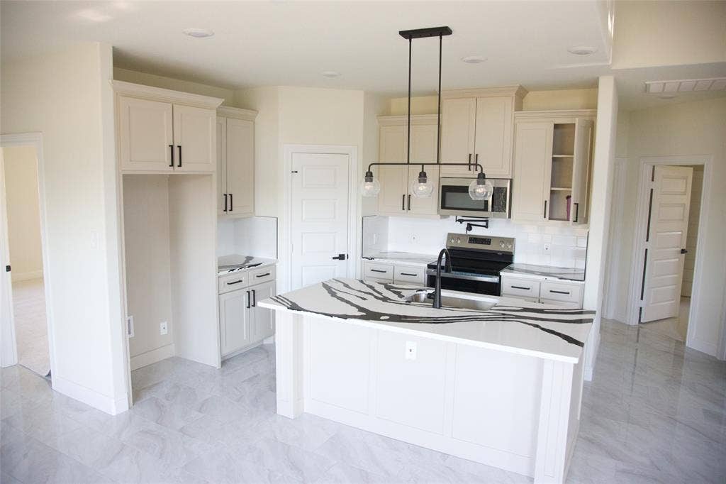 9432 PRAIRIEVIEW Drive, Crowley, TX 76134 Kitchen featuring a central island with a large countertop, white cabinetry with black hardware, stainless steel appliances, and light-toned flooring
