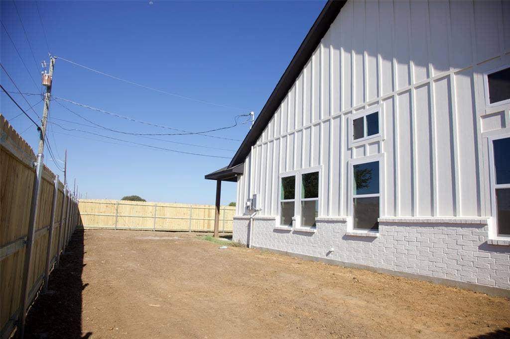 9432 PRAIRIEVIEW Drive, Crowley, TX 76134 White board and batten siding with contrasting dark trim, white brick foundation, multiple windows with white frames, and a wooden privacy fence