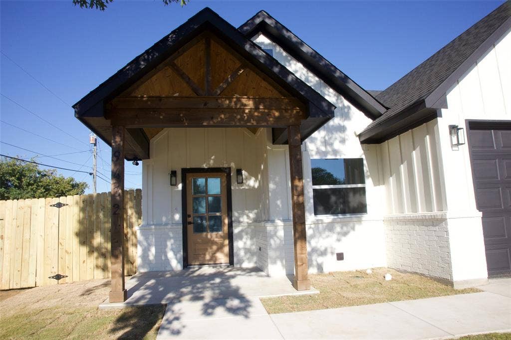 9432 PRAIRIEVIEW Drive, Crowley, TX 76134 Contemporary exterior featuring white board and batten siding, dark shingle roof, and a wood-finish entry door with multiple glass panes