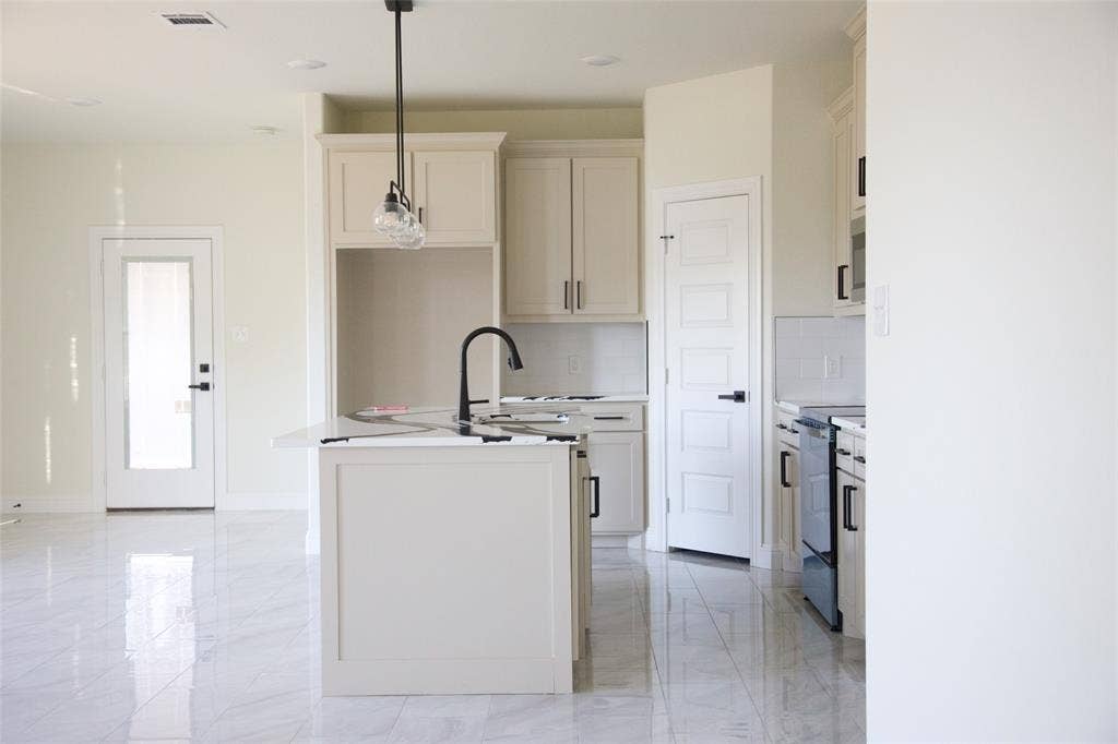 9432 PRAIRIEVIEW Drive, Crowley, TX 76134 Kitchen featuring an island with a built-in sink and matte black faucet, white cabinetry with black hardware, and an electric range