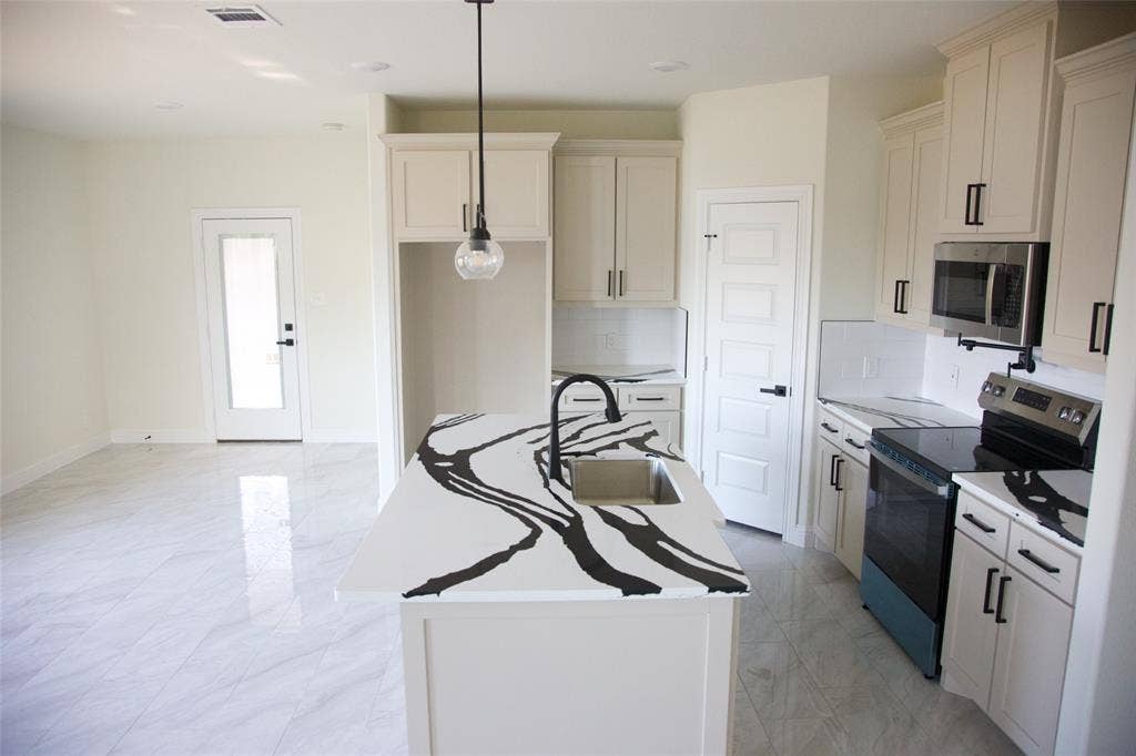 9432 PRAIRIEVIEW Drive, Crowley, TX 76134 Contemporary kitchen featuring a center island with an undermount sink, white cabinetry with dark hardware, a stainless steel microwave, and a black cooktop