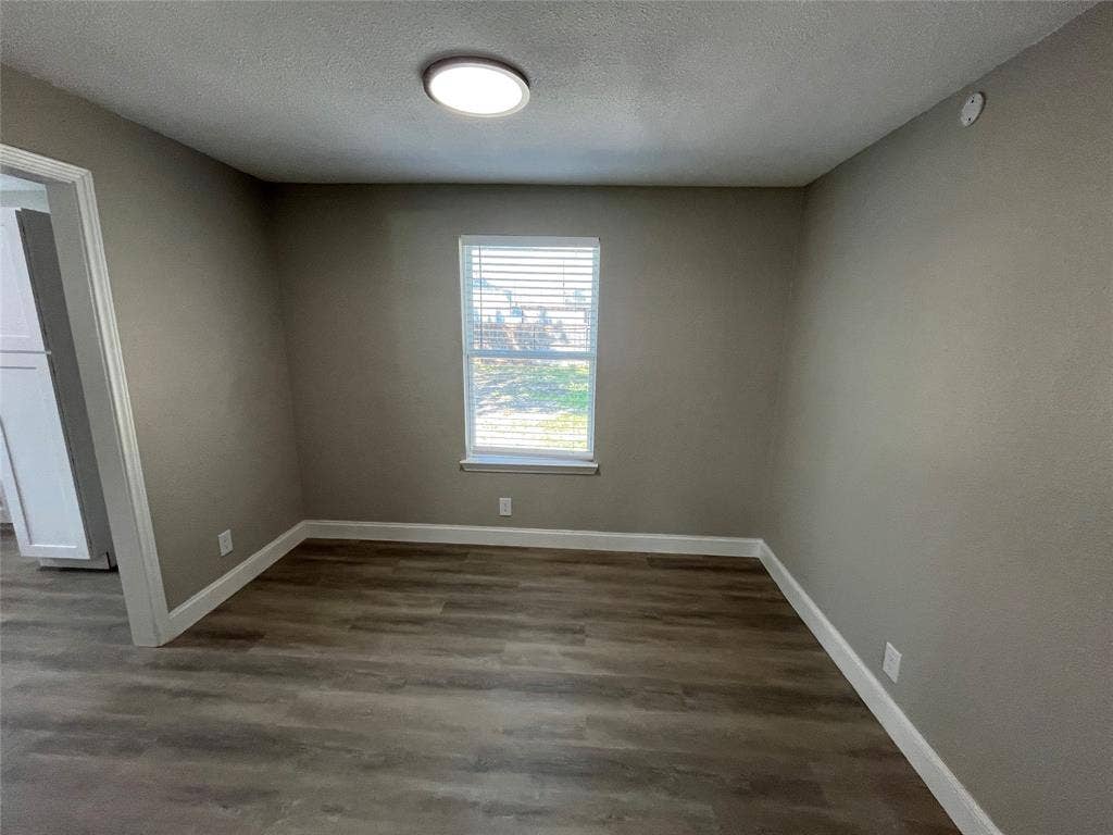622 Austin Street, Grand Prairie, TX 75051 Neutral-toned interior room featuring wood-finish flooring, a single window with integrated horizontal blinds, and a circular flush-mount ceiling light fixture