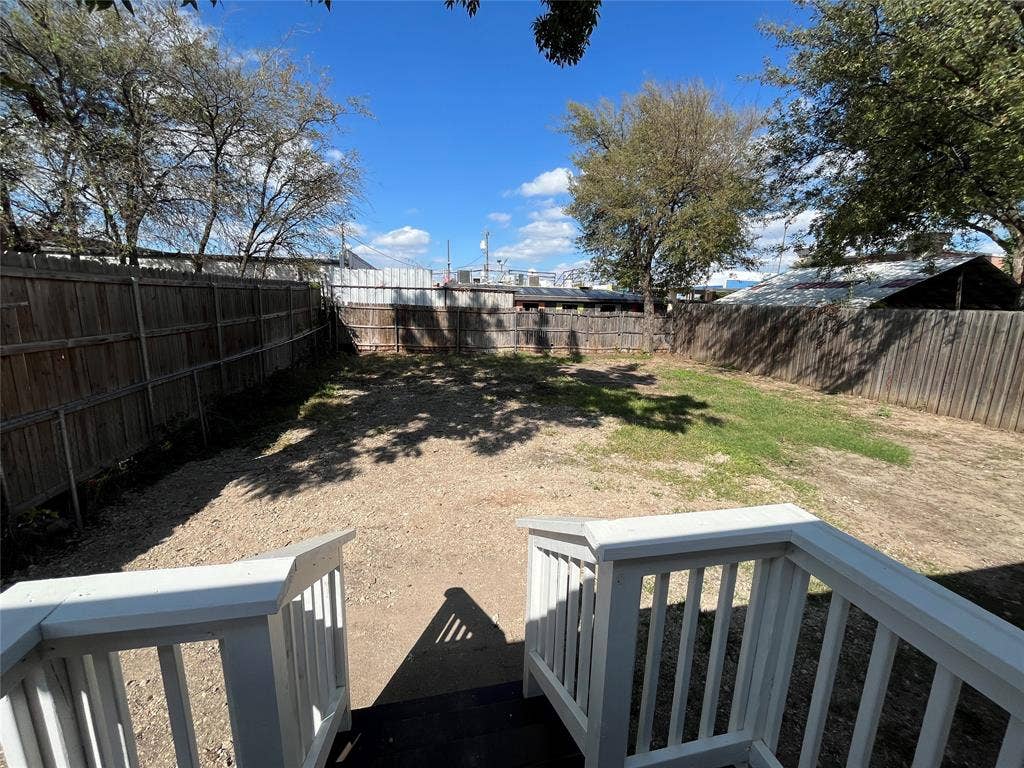 622 Austin Street, Grand Prairie, TX 75051 Backyard area enclosed by a wooden privacy fence, featuring a white-railed elevated deck and mature trees
