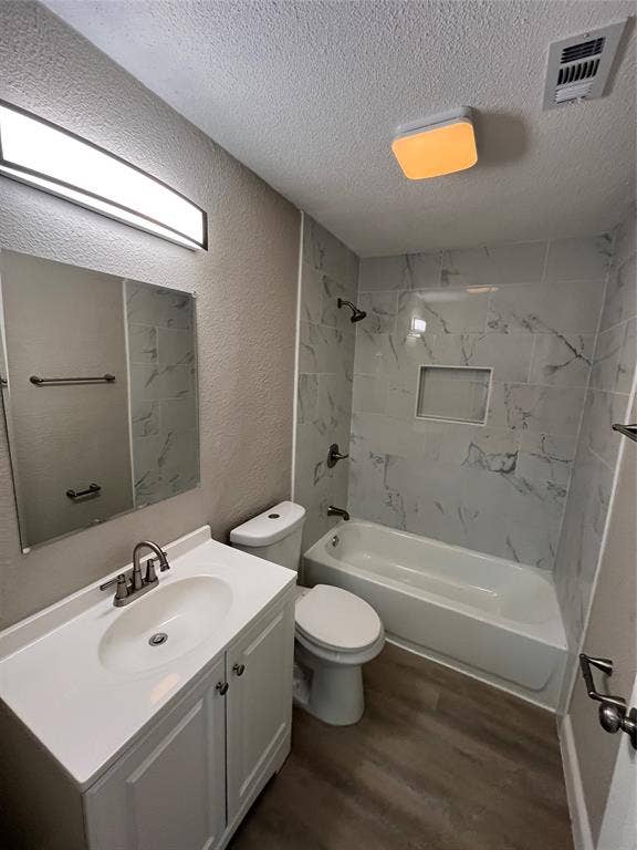 622 Austin Street, Grand Prairie, TX 75051 Bathroom featuring a vanity with a white countertop and oval under-mount sink, wood-finish flooring, and a tub-shower combination enclosed by large-format, light-toned tile with integrated shelving