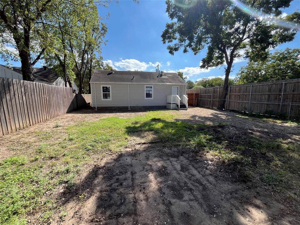 622 Austin Street, Grand Prairie, TX 75051 Rear exterior featuring light-toned horizontal siding, a pitched roofline, white exterior trim, and a fenced backyard with mature trees
