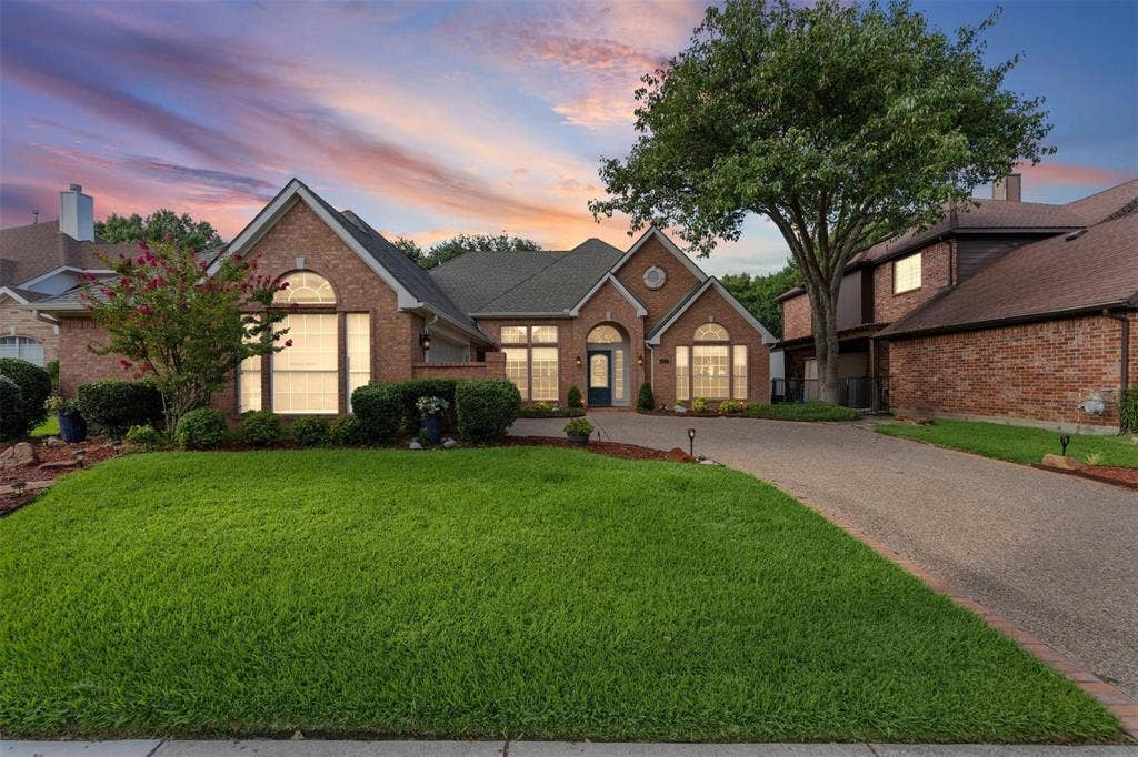 521 Palm Desert Drive, Garland, TX 75044 Brick exterior with arched windows, mature landscaping, a paved driveway, and an attached garage