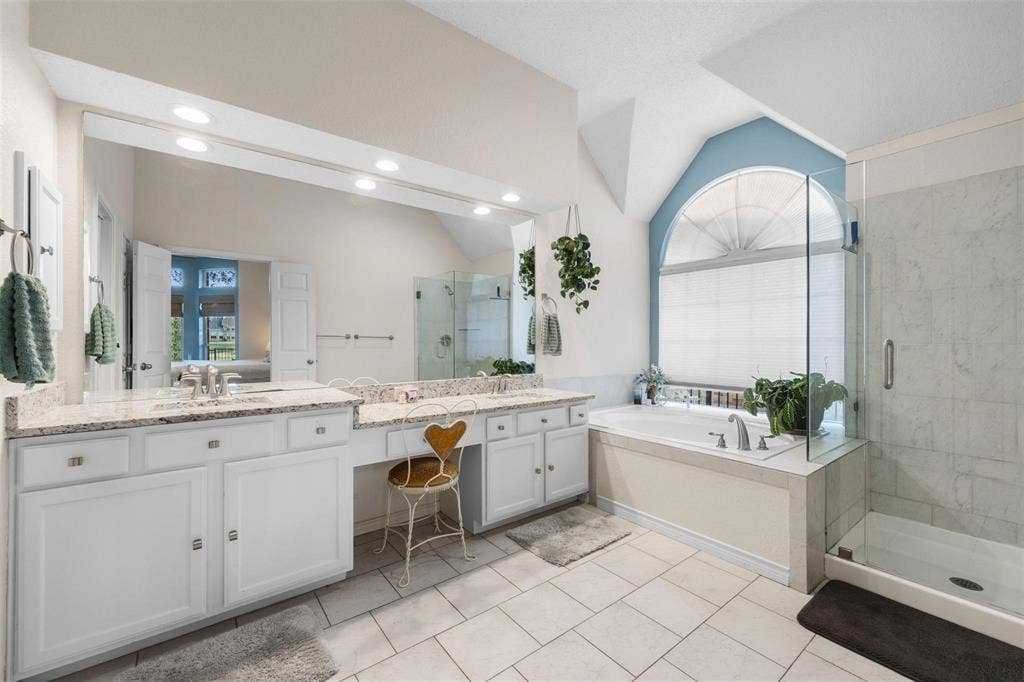 521 Palm Desert Drive, Garland, TX 75044 Dual vanity with light-toned countertops and undermount sinks, glass-enclosed shower, built-in soaking tub, and arched window