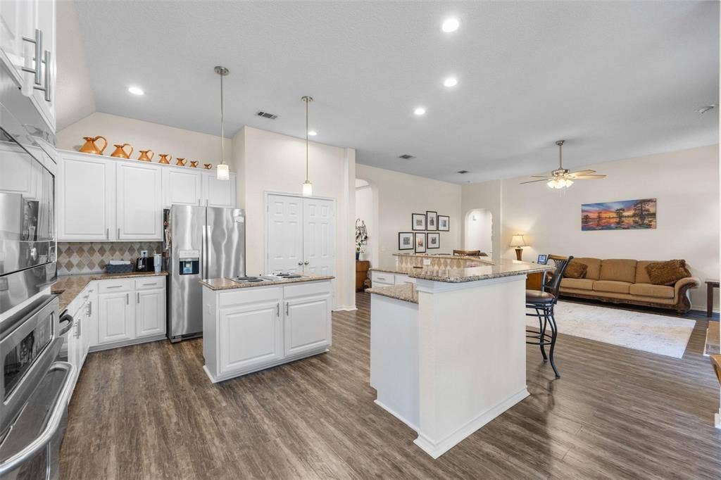 521 Palm Desert Drive, Garland, TX 75044 Kitchen with wood-finish flooring, white cabinetry, stainless steel appliances, and a central island with a granite countertop