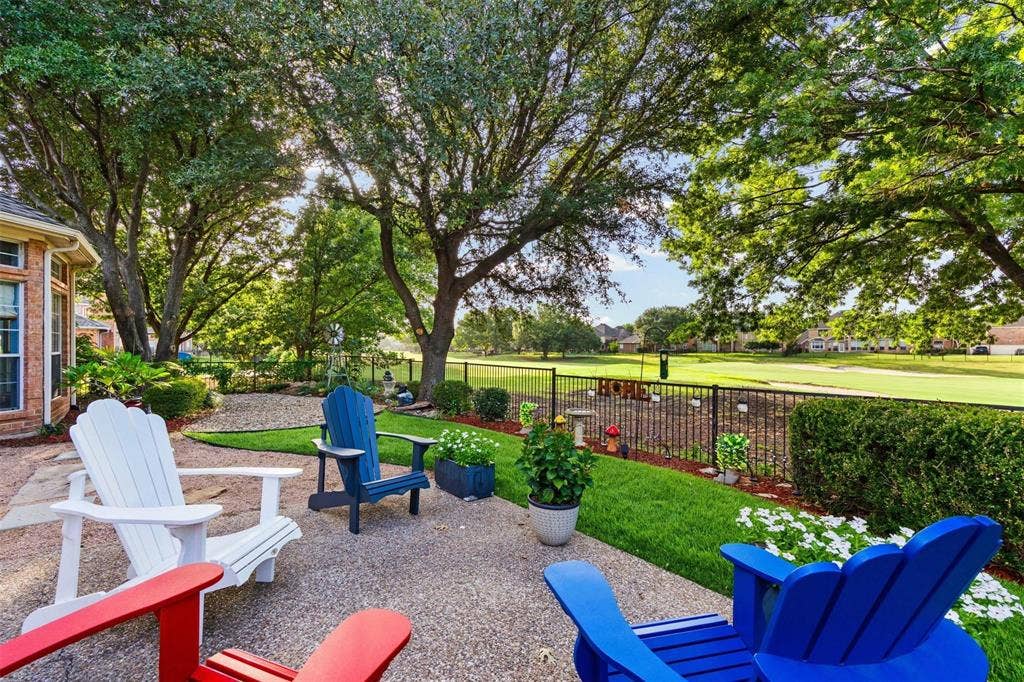 521 Palm Desert Drive, Garland, TX 75044 Expansive patio with a concrete surface, manicured lawn, and mature trees, bordered by a black metal fence