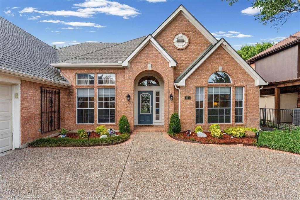 521 Palm Desert Drive, Garland, TX 75044 Brick exterior with a gabled roofline, arched entry, decorative front door, and mature landscaping
