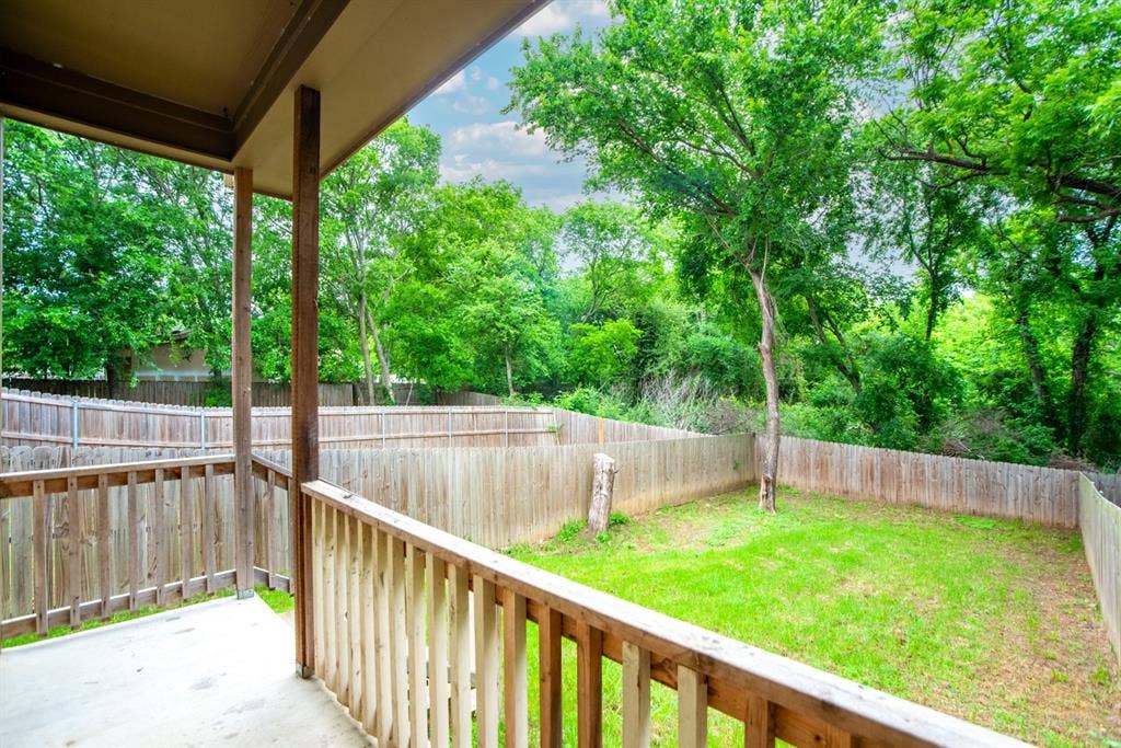 440 Pecan Hollow, Garrett, TX 75119 Covered patio with a concrete surface and wooden railing, overlooking a fenced backyard with a grass lawn and mature trees
