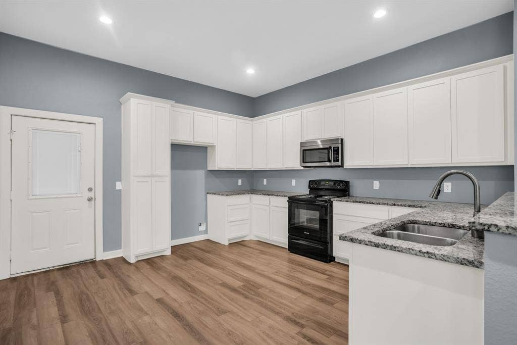 440 Pecan Hollow, Garrett, TX 75119 Kitchen featuring white cabinetry, wood-finish flooring, granite countertops, a stainless steel microwave, and a black range