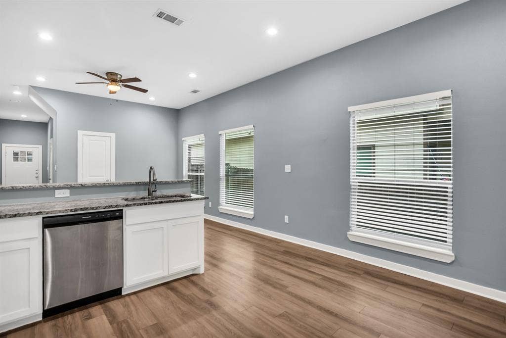 440 Pecan Hollow, Garrett, TX 75119 Kitchen island featuring a stainless steel dishwasher, undermount sink with a gooseneck faucet, white cabinetry, and a stone-finish countertop
