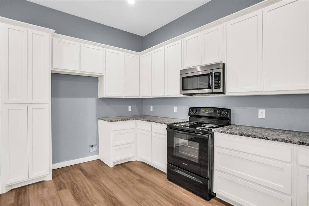 440 Pecan Hollow, Garrett, TX 75119 Kitchen featuring extensive white shaker cabinetry, speckled countertops, wood-finish flooring, a stainless steel microwave, and a black electric range