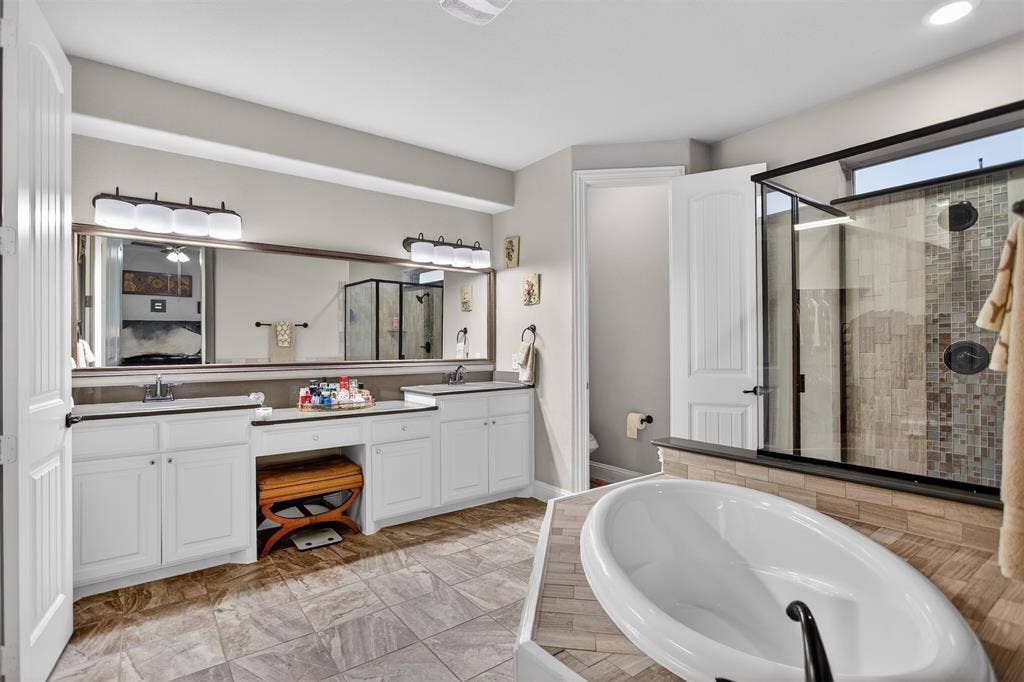 Freestanding soaking tub, walk-in shower with tile surround, double vanity with dual sinks, and large wall-mounted mirror