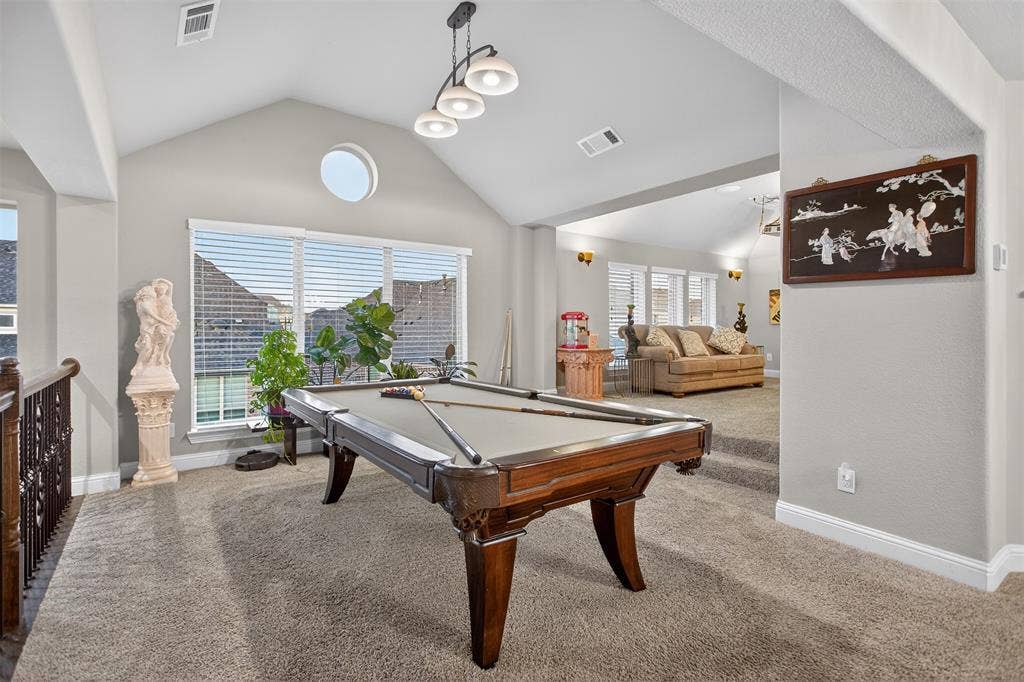Vaulted ceiling with modern chandelier, round accent window, wall of windows with blinds, and carpeted flooring