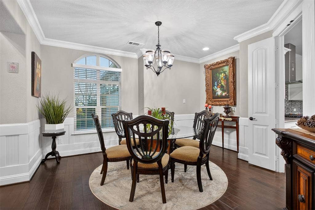 Hardwood flooring, arched window, paneled wainscoting, crown molding, and chandelier lighting