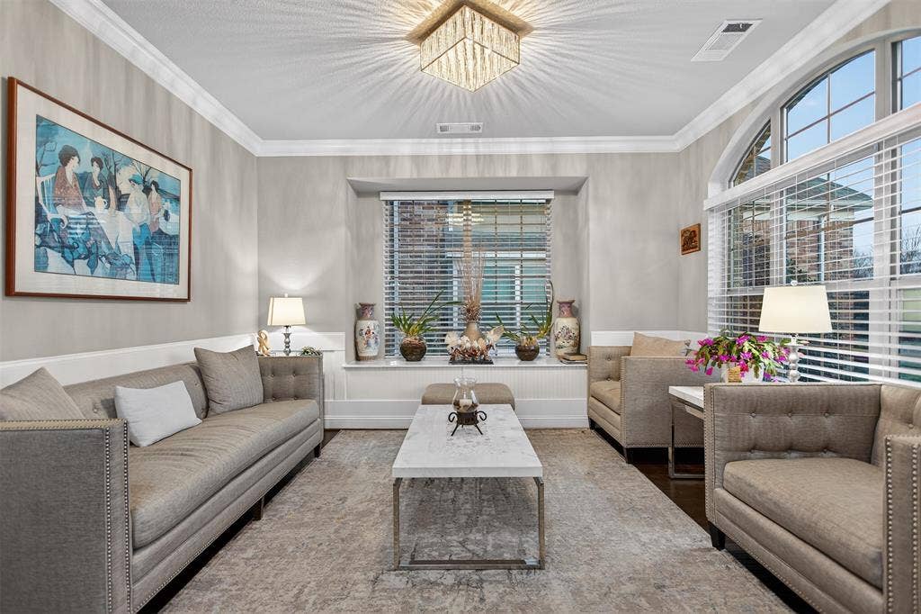 Living area featuring a crystal chandelier, crown molding, arched windows, and wainscoting