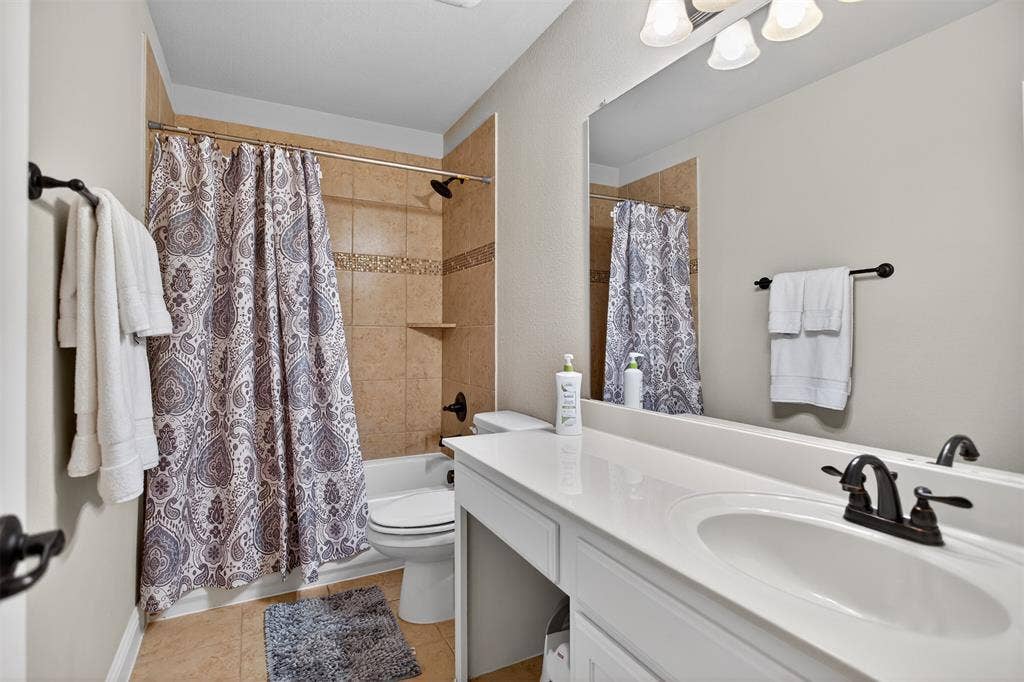 Full-size mirror, integrated vanity lighting, white countertop, dark bronze-finish fixtures, and tile flooring