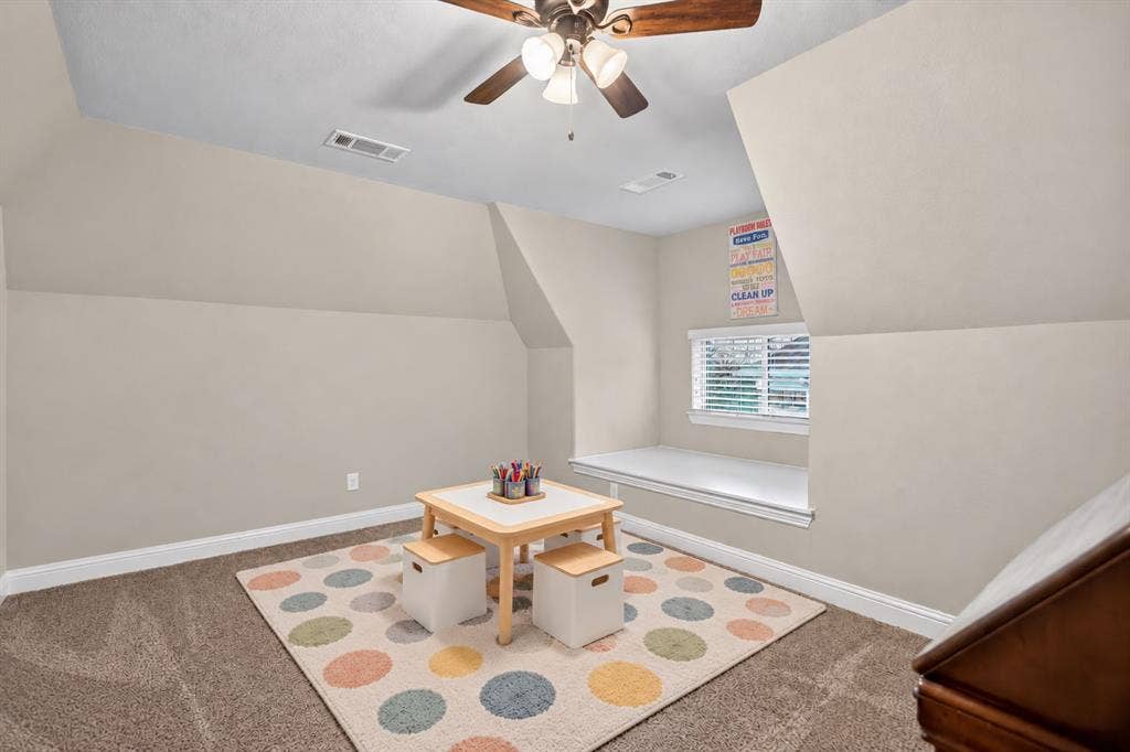Carpeted flooring, sloped ceilings, ceiling fan with integrated lighting, window with blinds, and a built-in window seat