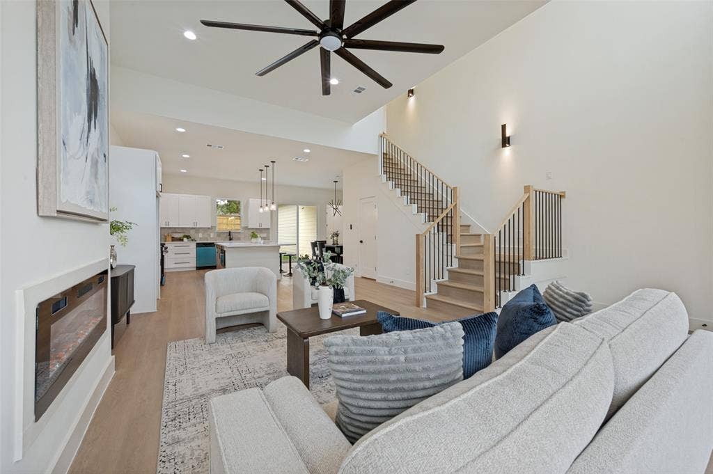 1511 Morrell Avenue, Dallas, TX 75203 Spacious living area featuring a modern fireplace, high vaulted ceilings, wood-finish flooring, a contemporary ceiling fan, and a staircase with wood handrails and black iron balusters