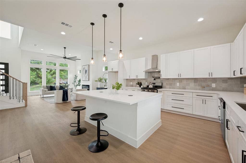 1511 Morrell Avenue, Dallas, TX 75203 Expansive open concept living space featuring wood-finish flooring, a contemporary kitchen with a large island, stainless steel appliances, and white cabinetry, complemented by a living area with a fireplace and large windows