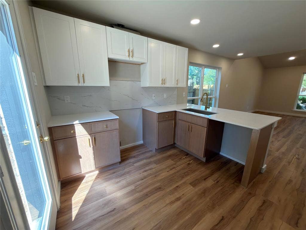 1834 Caldwell, Garland, TX 75041 Modern kitchen featuring white upper cabinetry, wood-finish lower cabinetry, light-toned countertops, a white tile backsplash, and wood-finish flooring