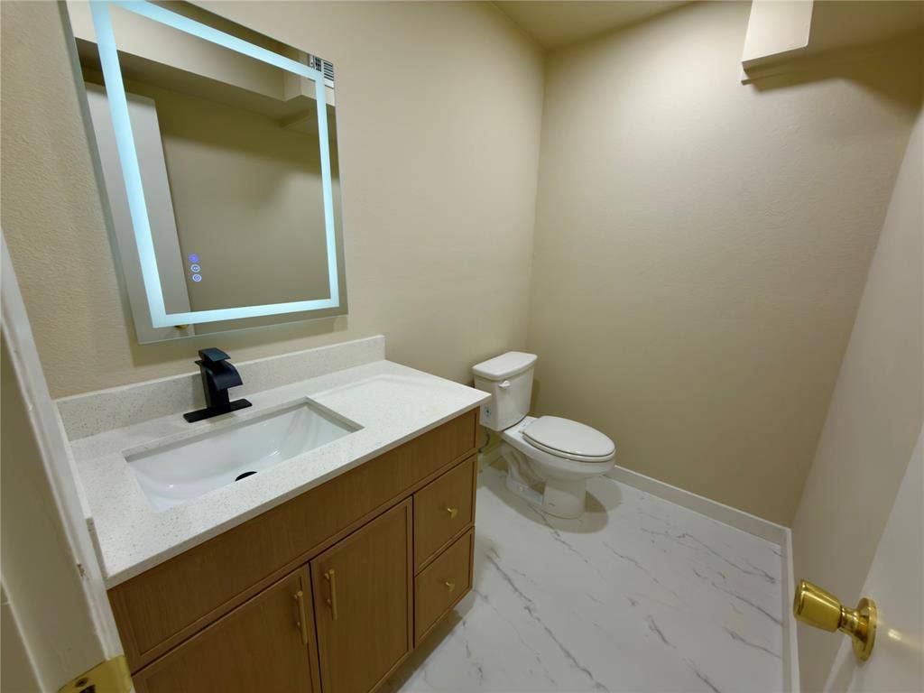 1834 Caldwell, Garland, TX 75041 Vanity with integrated sink, modern black faucet, illuminated mirror, and marble-look flooring