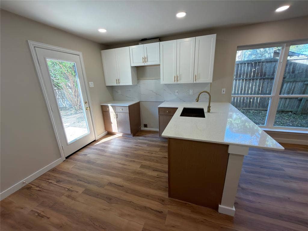 1834 Caldwell, Garland, TX 75041 Kitchen featuring an island with a built-in sink, white cabinetry with gold-tone hardware, wood-finish flooring, recessed lighting, and a glass-paneled exterior door
