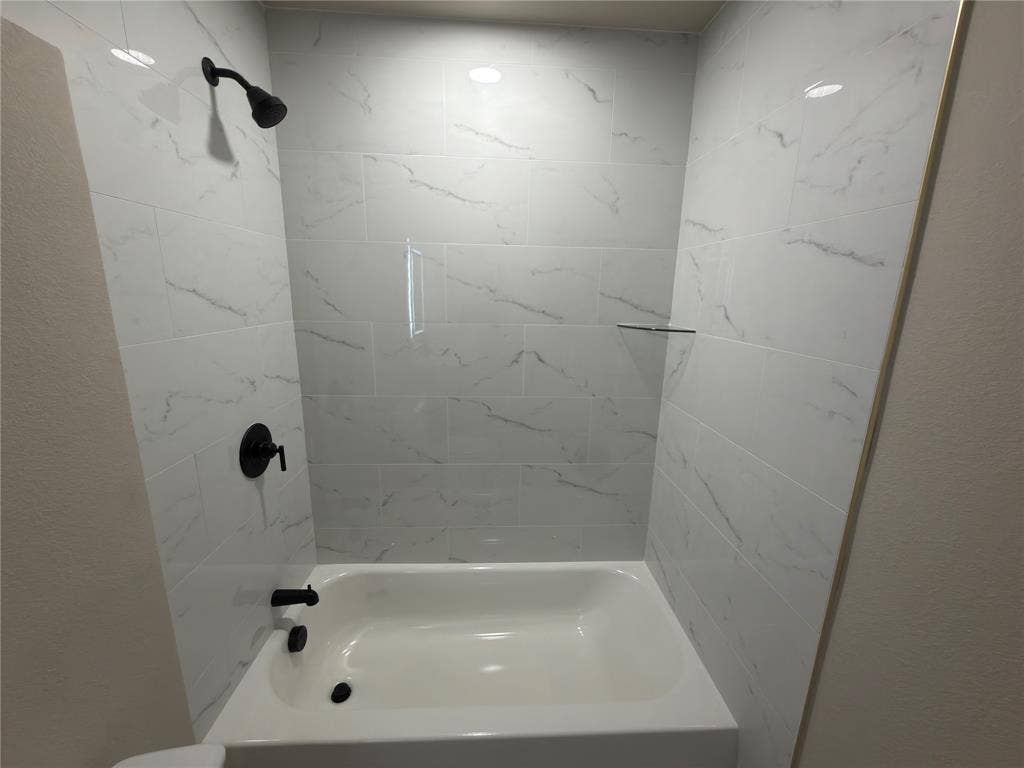 1834 Caldwell, Garland, TX 75041 Bathtub with white tiled surround, matte black shower fixtures, and recessed glass shelf