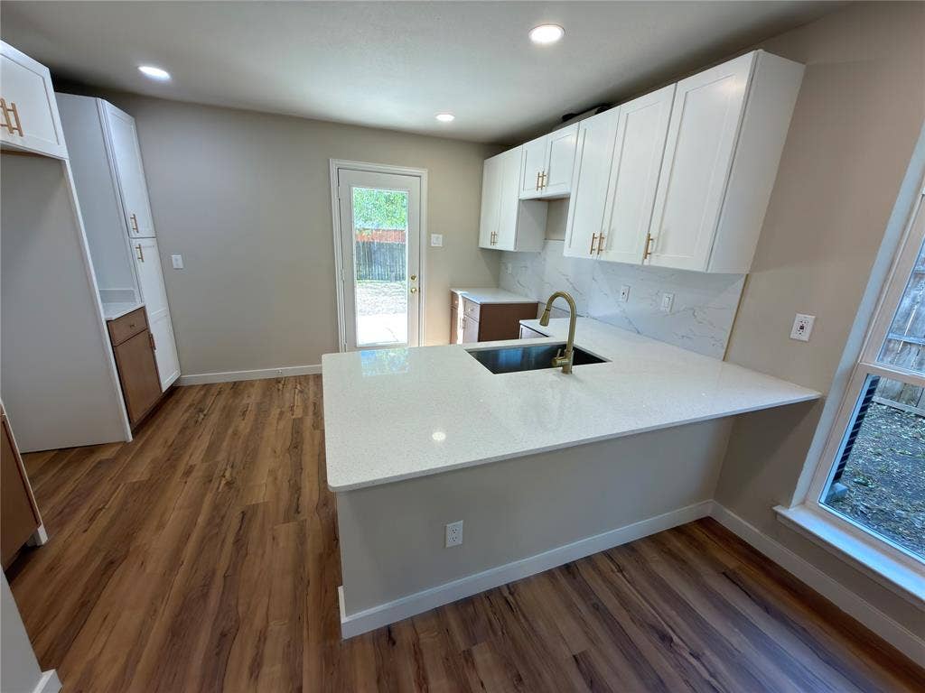 1834 Caldwell, Garland, TX 75041 Kitchen featuring white shaker cabinetry, wood-finish flooring, recessed lighting, a kitchen island with an undermount sink, and a full backsplash