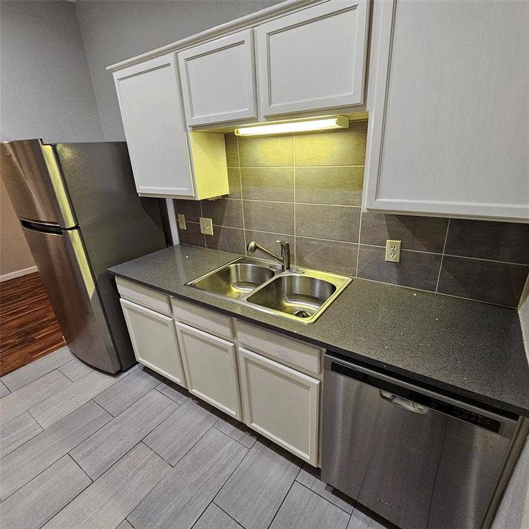 9600 ROYAL, #612, Dallas, TX 75243 Kitchen with appliances with stainless steel finishes, wood finish floors, white cabinets, backsplash, and dark countertops