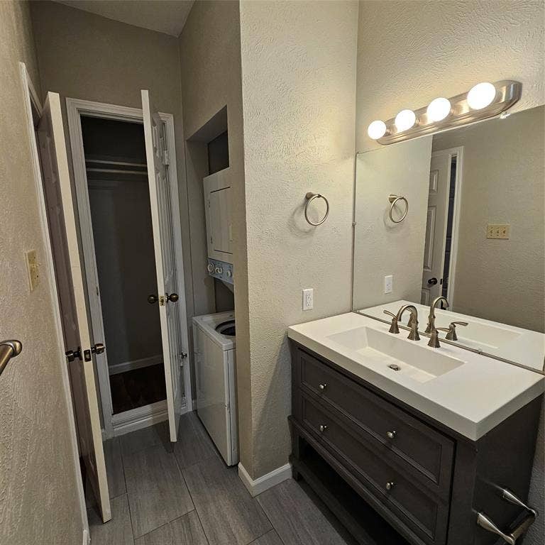 9600 ROYAL, #612, Dallas, TX 75243 Bathroom with vanity, wood finished floors, a textured wall, and stacked washing machine and dryer
